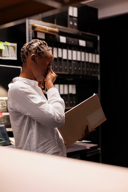 Kostenloses Foto Überarbeitete polizistin mit augenschmerzen beim lesen des detektivberichts in der nacht. erschöpfter afroamerikanischer privatdetektiv, der sich die nase reibt und den kriminalfall spät untersucht