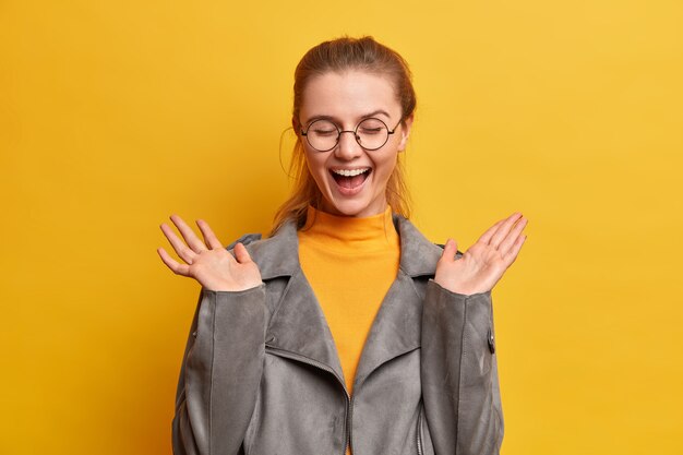 Kostenloses Foto Überglückliche teenagerin lacht glücklich, hält die hände hoch und schließt die augen vor befriedigung