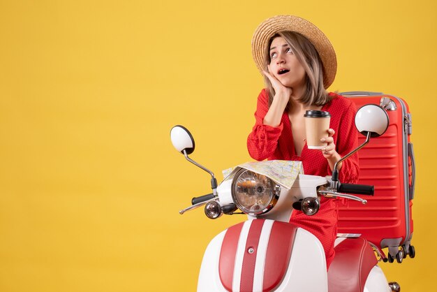 überraschte junge Dame im roten Kleid mit Kaffeetasse in der Nähe von Moped