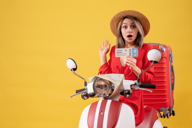 überraschte junge Dame im roten Kleid mit Ticket auf dem Moped