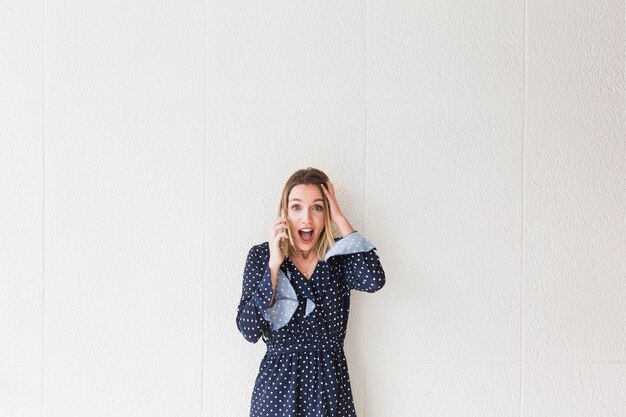 Kostenloses Foto Überraschte junge frau, die gegen die wand spricht am handy steht