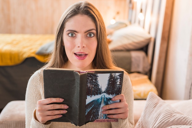 Überraschte junge Frau, die in der Hand Buch hält