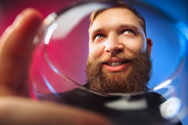 überraschter junger Mann posiert mit einem Glas Wein. Emotionales männliches Gesicht. Blick aus dem Glas.