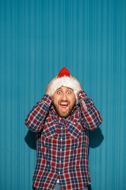 überraschter Mann, der eine Weihnachtsmütze auf blauem Hintergrund trägt