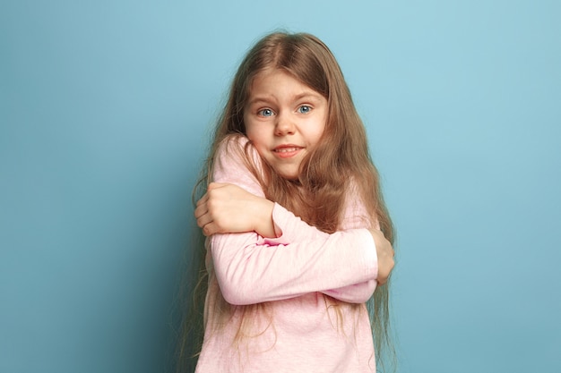 überraschtes jugendlich Mädchen auf einem blauen Studiohintergrund. Gesichtsausdrücke und Menschen Emotionen Konzept.