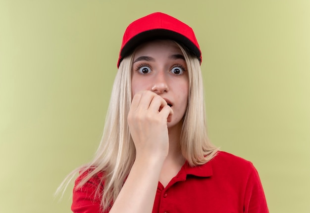 Kostenloses Foto Überraschtes junges mädchen der lieferung, das rotes t-shirt in der kappe trägt, legte ihre hand auf mund auf lokalisiertem grünem hintergrund