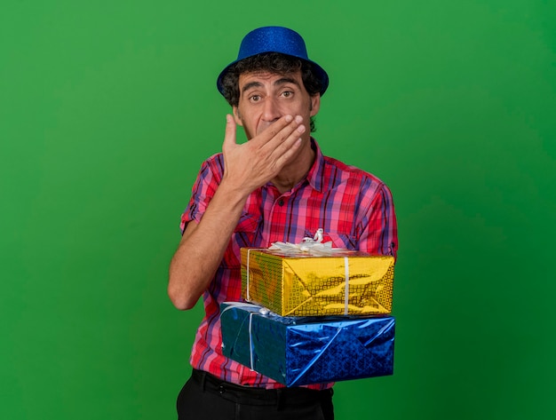 Kostenloses Foto Überraschtes kaukasisches partei-mann mittleren alters, das parteihut hält, der geschenkverpackungen hält, die hand auf mund halten, betrachten kamera lokalisiert auf grünem hintergrund mit kopienraum