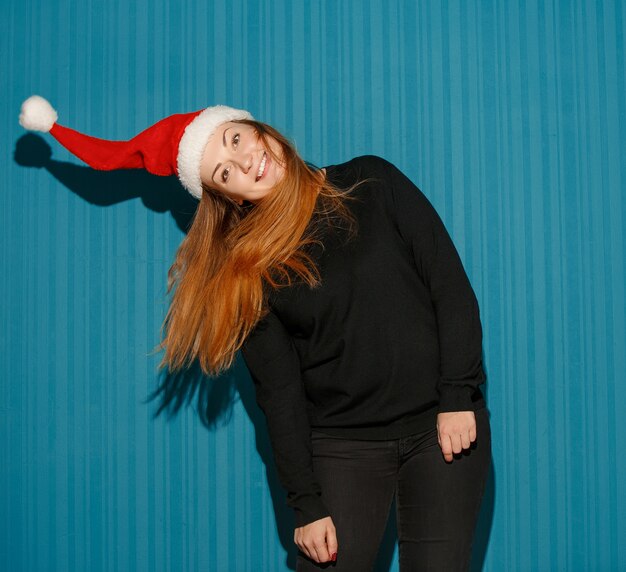 Kostenloses Foto Überraschtes weihnachtsmädchen, das eine weihnachtsmütze auf dem blauen studiohintergrund trägt