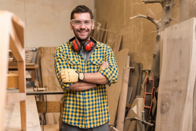 Überzeugter glücklicher Tischler mit seinem Arm kreuzte die Stellung in der Werkstatt