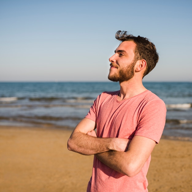 Kostenloses Foto Überzeugter junger mann mit seinen armen kreuzte die stellung am strand