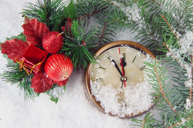 Uhr mit tannenzweigen und weihnachtsdekoration unter schnee hautnah