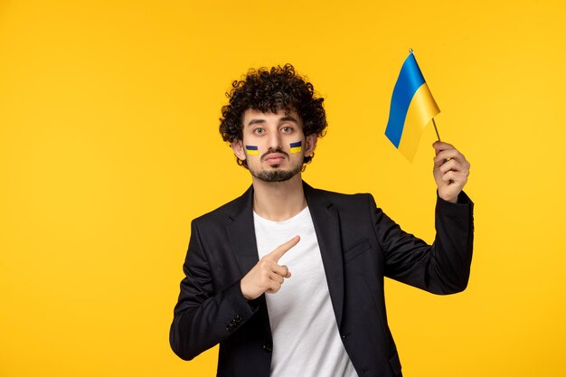 Ukraine-Russland-Konflikt junger Mann im Blazer bemalte ukrainische Flagge auf dem Gesicht, das auf die Flagge zeigt