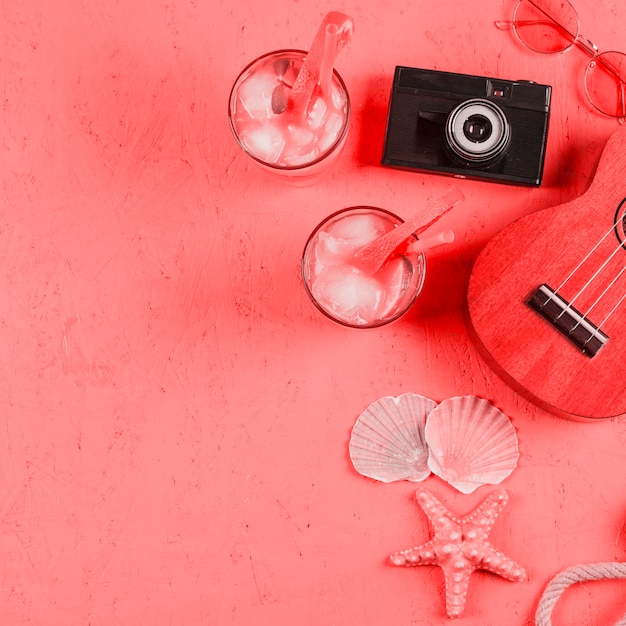 Kostenloses Foto ukulele; sonnenbrille; muscheln; kamera- und cocktailgläser auf strukturiertem korallenhintergrund