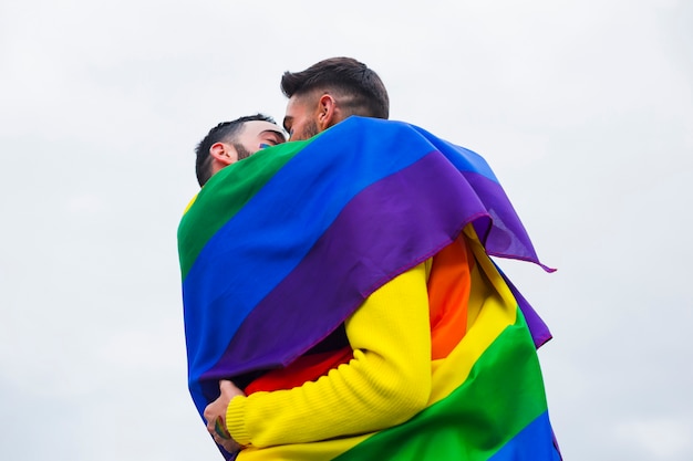 Umarmende Gays beim Abdecken der Regenbogenflagge