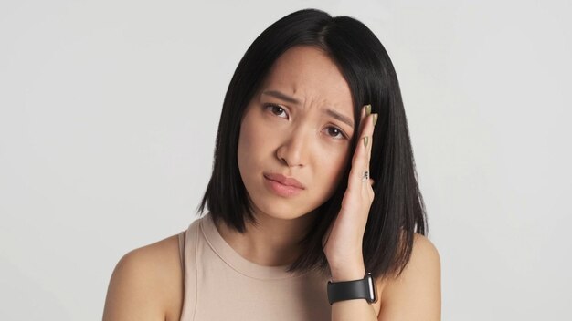 Umgekippte asiatische Frau, die Kamera über weißem Hintergrund schuldig betrachtet Trauriger Ausdruck