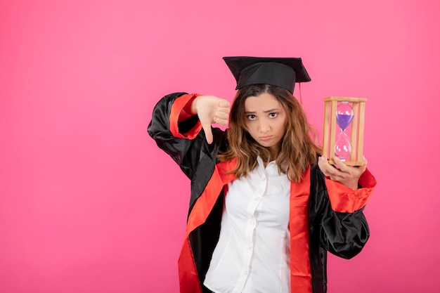 Umgekippte Studenten, die Sanduhr halten und Daumen nach unten gestikulieren. Foto in hoher Qualität