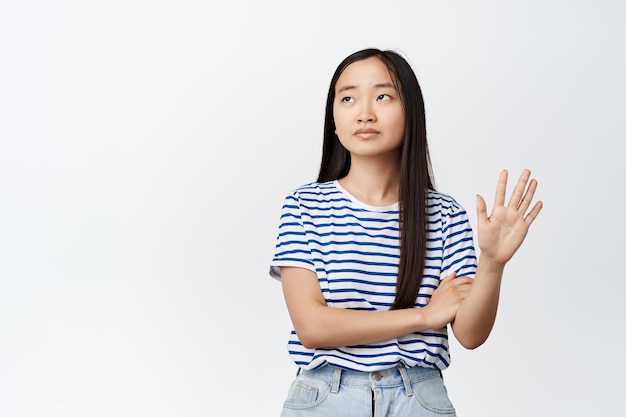 Unamüsiertes arrogantes asiatisches Mädchen, das eine Handgeste zeigt, die mit Abneigung wegschaut und etwas ablehnt, zeigt weißen Hintergrund des Ablehnungszeichens