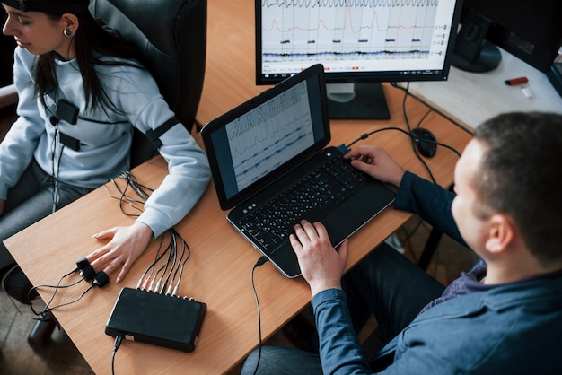 Unehrlichkeitskonzeption. Mädchen geht Lügendetektor im Büro vorbei. Fragen stellen. Polygraphentest