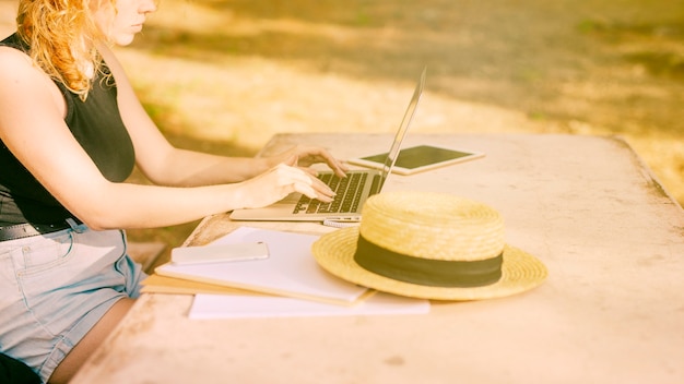 Unerkennbare frau, die am schreibtisch sitzt und draußen an laptop arbeitet