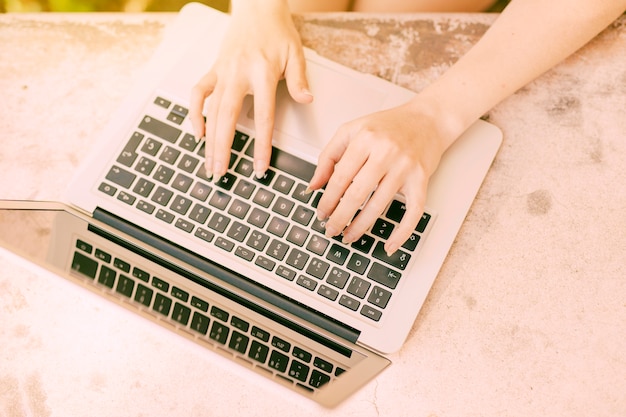 Kostenloses Foto unerkennbare frau, die draußen auf laptoptastatur schreibt