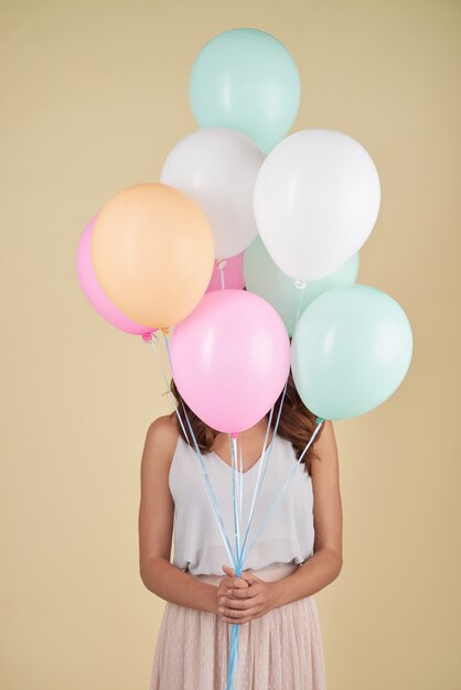 Unerkennbare Frau, die im Studio mit ihrem Gesicht bedeckt mit Ballonen aufwirft