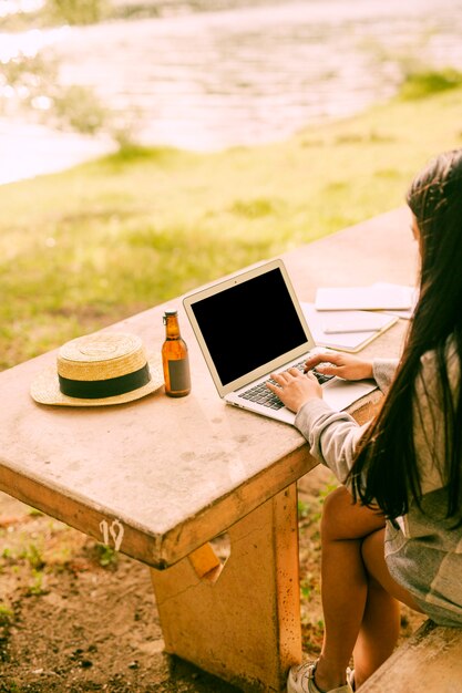 Kostenloses Foto unerkennbare frau, die laptop außerhalb des nahen sees verwendet