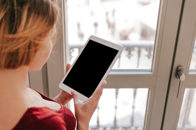 Kostenloses Foto unerkennbare frau mit tablette nahe fenster