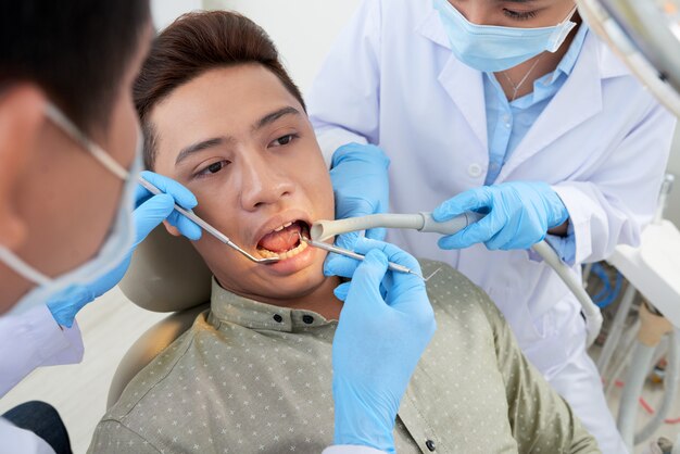 Unerkennbarer asiatischer Zahnarzt und Krankenschwester, welche die Zähne des männlichen Patienten überprüft