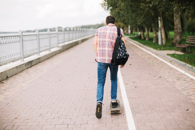 Unerkennbarer Jugendlicher, der nahe Fahrradweg Skateboard fährt