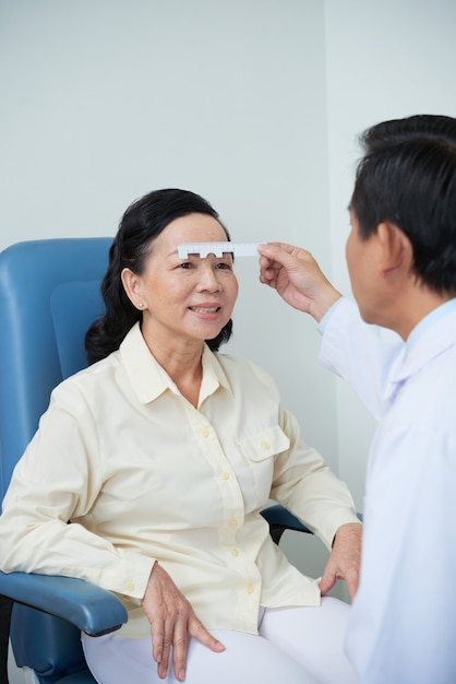 Unerkennbarer männlicher Augenarzt, der Sehkraftprüfung für asiatischen weiblichen Patienten durchführt