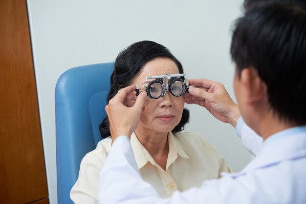Unerkennbarer männlicher Augenarzt, der Versuchslinsenrahmen für älteren weiblichen Patienten passt