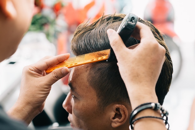Kostenloses Foto unerkennbarer männlicher friseur, der das haar des kunden mit trimmer und kamm schneidet
