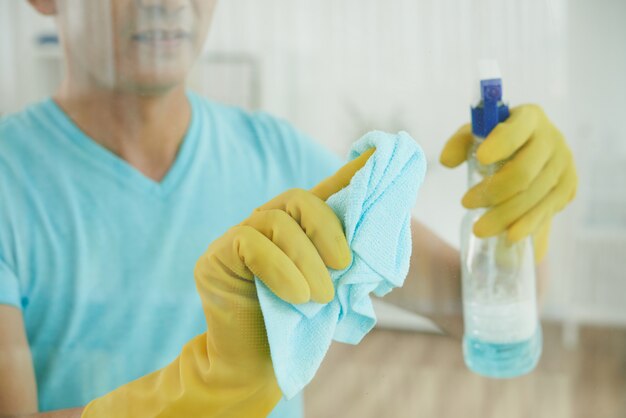 Unerkennbarer Mann in den Handschuhen, die Fenster mit Reinigungsflüssigkeit sprühen und mit Stoff abwischen