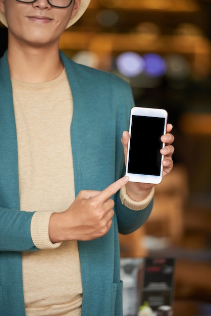 Unerkennbarer stilvoller Mann, der im Café steht, Smartphone hält und auf Schirm zeigt