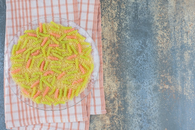 Ungebackene Fusilli-Nudeln in der Glasschüssel, auf Handtuch, auf dem Marmorhintergrund.