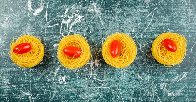 Ungekochte Capellini-Nudeln und Tomaten, auf dem Blau.