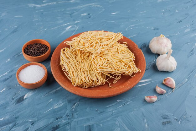 Ungekochte Instantnudeln mit frischem Knoblauch und Gewürzen auf einem blauen Tisch.