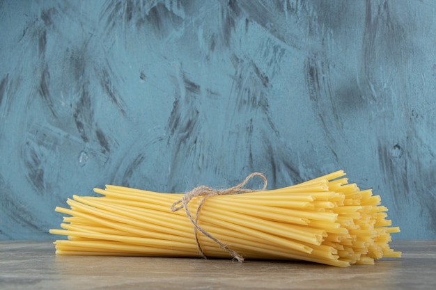 Ungekochte Rohrspaghetti mit Seil auf Marmoroberfläche gebunden