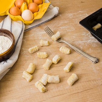 Ungekochte selbst gemachte kartoffelgnocchi mit gabel über holztisch mit mehl und eiern