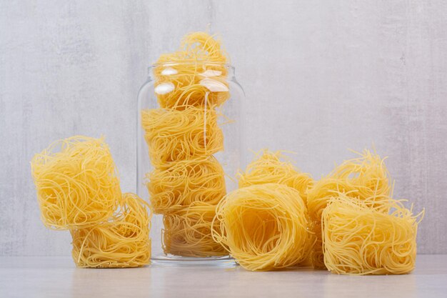 Ungekochte Spaghetti-Nester auf Marmortisch mit Glas.