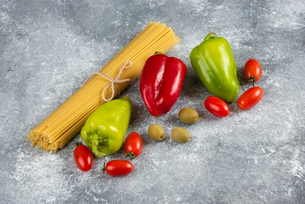 Ungekochte Spaghetti und verschiedenes Gemüse auf Steinoberfläche.