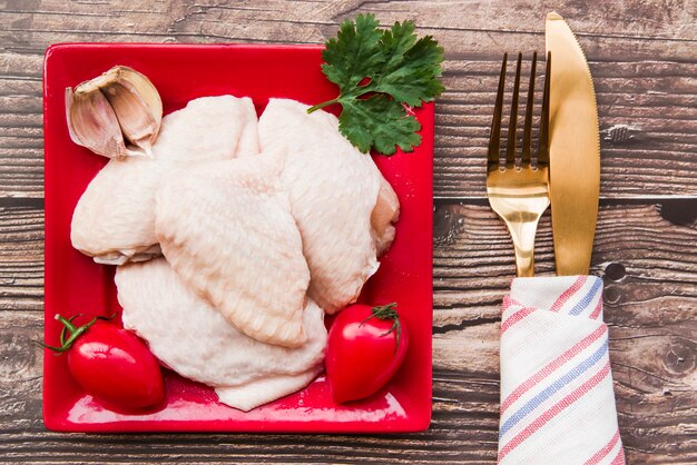 Ungekochtes Fleisch und Zutaten in der Platte mit goldenem Gabel- und Buttermesser