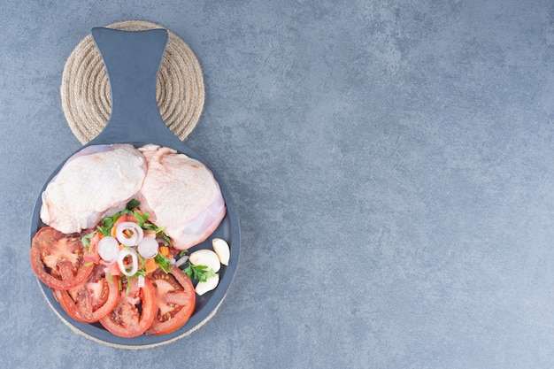 Ungekochtes Hähnchenfilet mit Tomatenscheiben auf dunklem Brett.