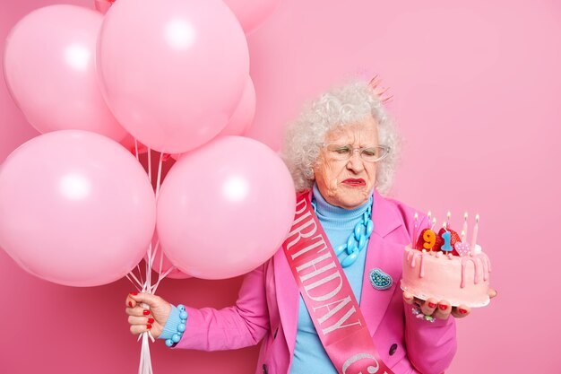Unglückliche ältere schöne Frau, die traurig darüber ist, älter zu werden, sieht köstlichen Kuchen mit brennenden Kerzen an und feiert den 91. Geburtstag. Alterungskonzept