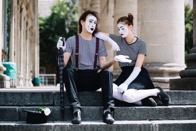 Unglücklicher männlicher und weiblicher Pantomimekünstler, der auf Treppenhaus sitzt
