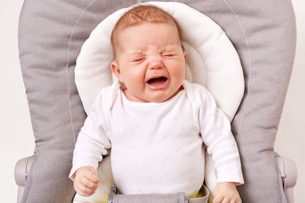 Unglückliches kleines Säuglingsmädchen oder -junge, der im Türsteherstuhl weint