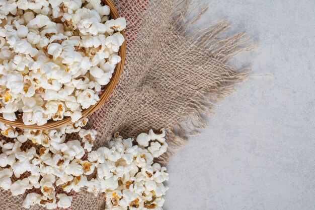 Unordentlicher Haufen Popcorn neben einer vollen Schüssel auf einem Stoffstück auf Marmor.