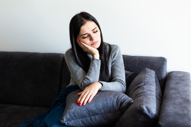 Unpässliche kranke Frau spürt ihre Temperatur, während sie zu Hause auf dem Sofa ruht