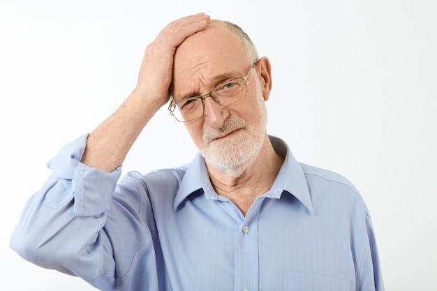 unrasierter älterer Geschäftsmann in rechteckiger Brille und formellem Hemd mit schrecklichen Kopfschmerzen oder Migräne, gestresst wegen Arbeitsproblemen, mit schmerzhaftem Ausdruck
