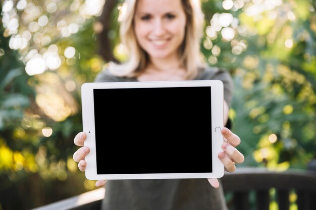 Unscharfe Frau, die Tablette im Park zeigt